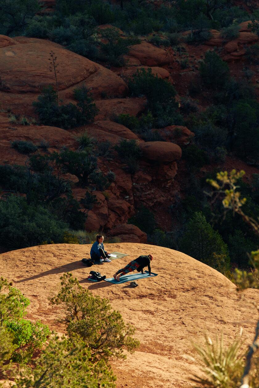 Two people do yoga in the Bell Rock area with canyon views in front of them. 