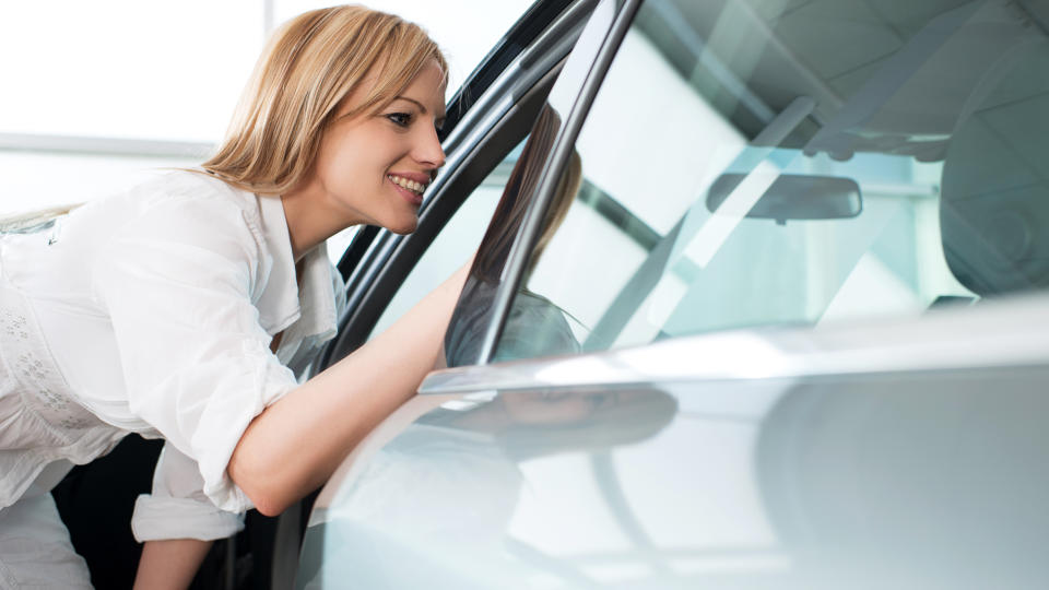 Mid adult woman looking through a opened window of a car in a showroom.