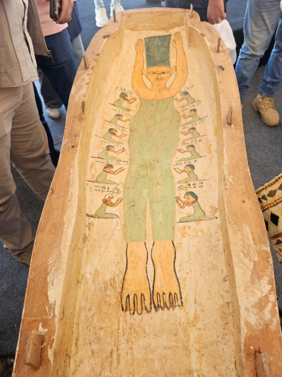 The coffin features an outline of a person with several kneeling figures beside it