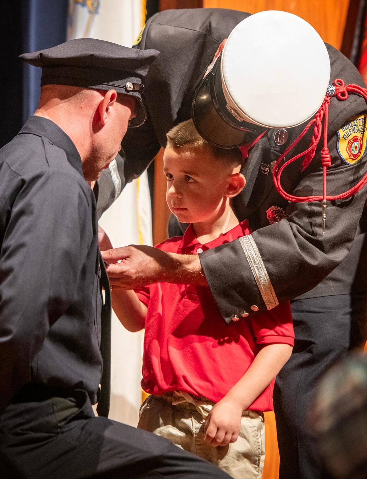 Newly sworn firefighter Justin Anger has his badge pinned on by his father, Worcester Fire Capt. David Anger, and his son Caleb during the Worcester Fire Department recruit class graduation ceremony Friday at Worcester Technical High School. His brother Tyler was also pinned by his father and grandfather at the ceremony.