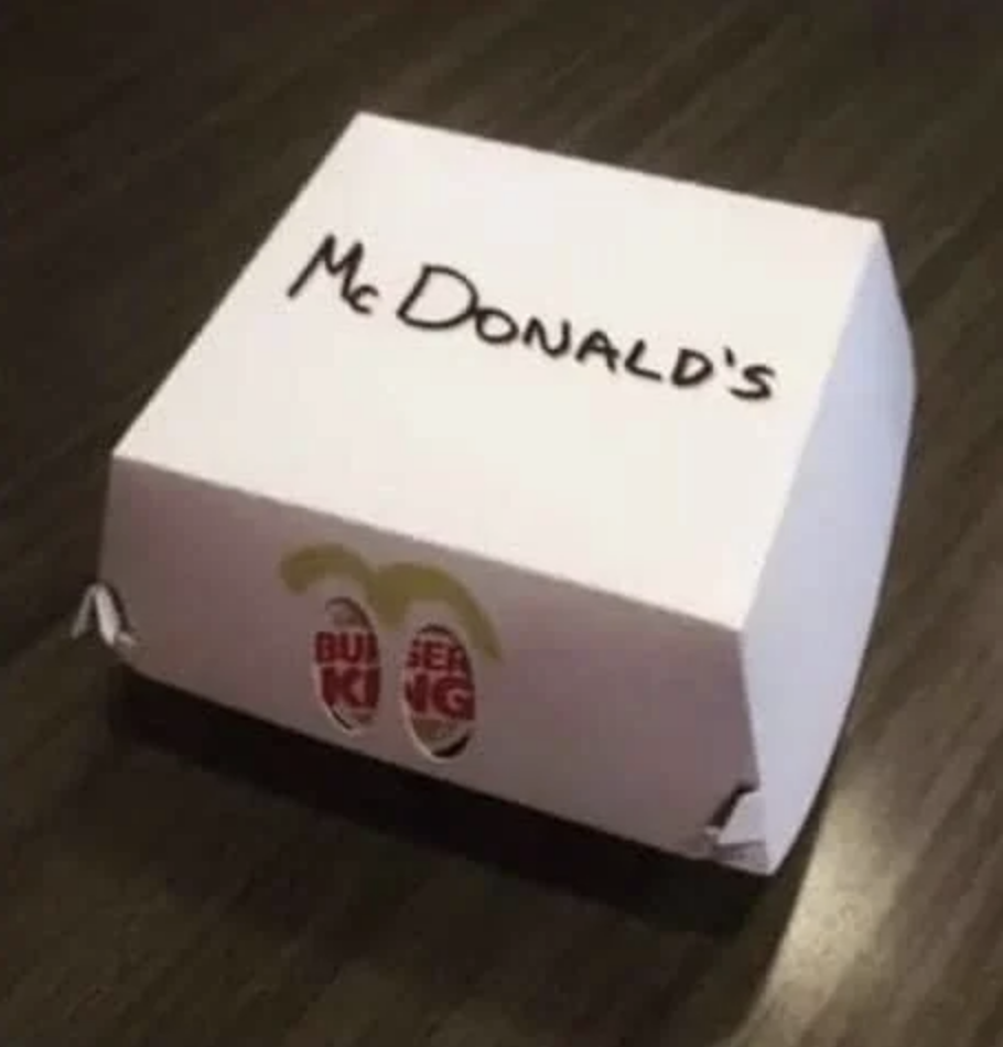 A takeout box with "McDonald's" written on it, with the Burger King logo visible through two "eye" holes