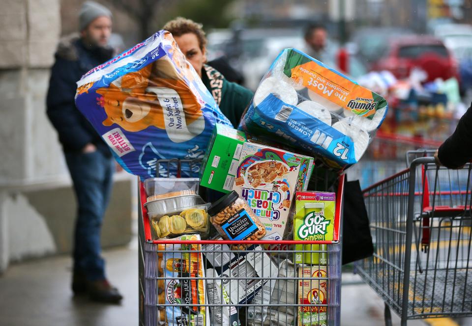 A person is seen behind a shopping cart piled high with goods.