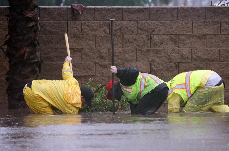 Workers attempt to unclog a drain on a flooded street as Tropical Storm Hilary moves through the area on August 20, 2023 in Rancho Mirage, California.