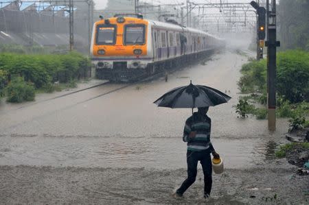 A man carrying an umbrella walks past a passenger train that moves through a water-logged track during heavy rains in Mumbai, July 9, 2018. REUTERS/Francis Mascarenhas