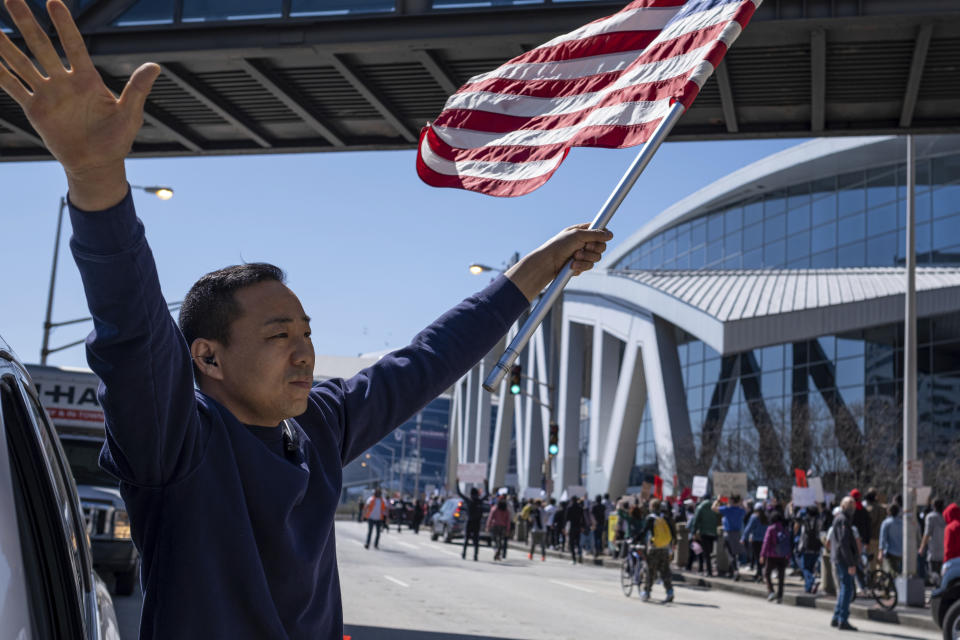 Hailun Song waves a U.S. flag and cheers marchers as a "stop Asian hate" rally in downtown Atlanta passes by Saturday afternoon, March 20, 2021. (AP Photo/Ben Gray)