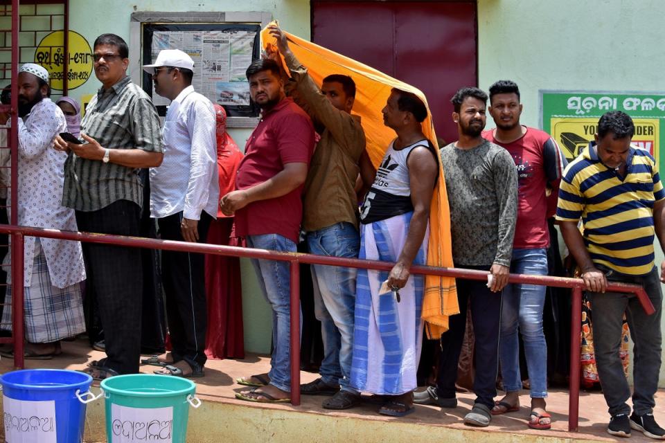 Men use a stole to cover from heat as they wait in a line outside a polling station to cast their votes during the sixth phase of India's general election, on a hot summer day in Bhubaneswar, India (REUTERS)