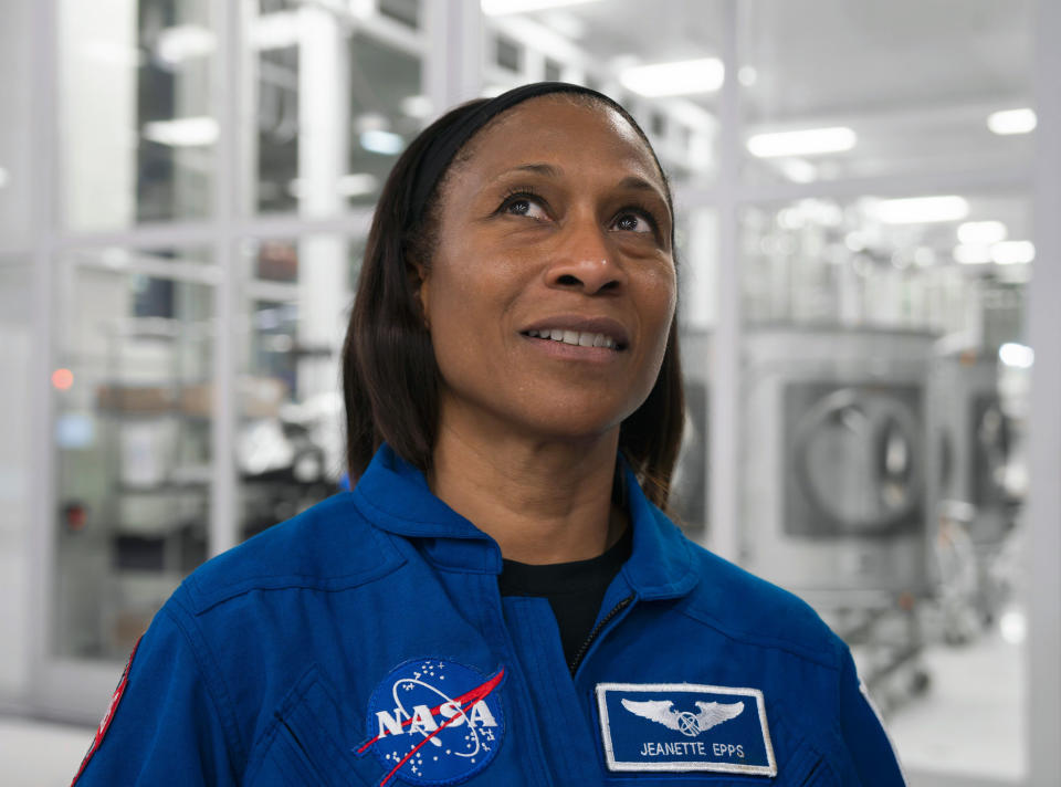 a woman in a blue dress staring up into the distance excitingly.  she is standing in a white room with many glass panels.