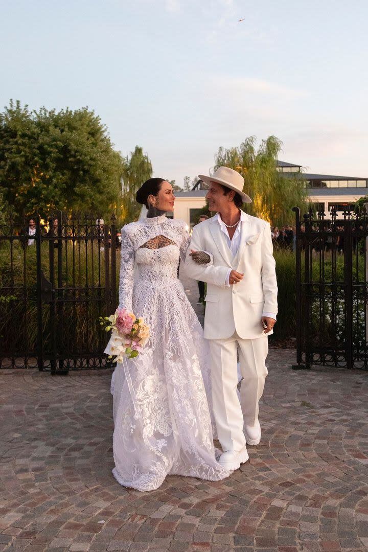 Con look total white, Cande Tinelli y Coti Sorokin posan para las cámaras tomados del brazo; ella lleva un ramo de flores en tonos pastel