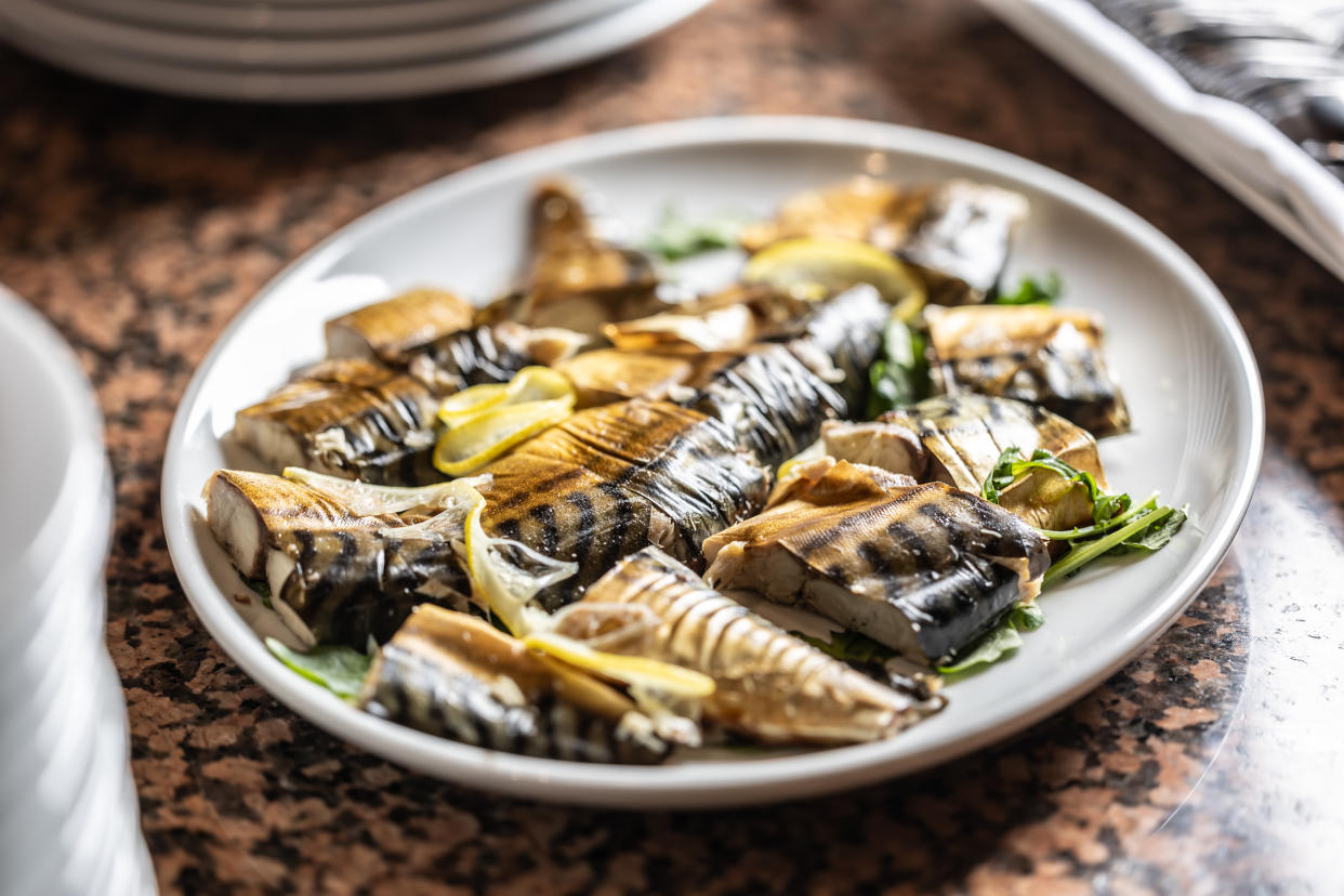 Smoked mackerel portioned on a plate with lemon and herbs.