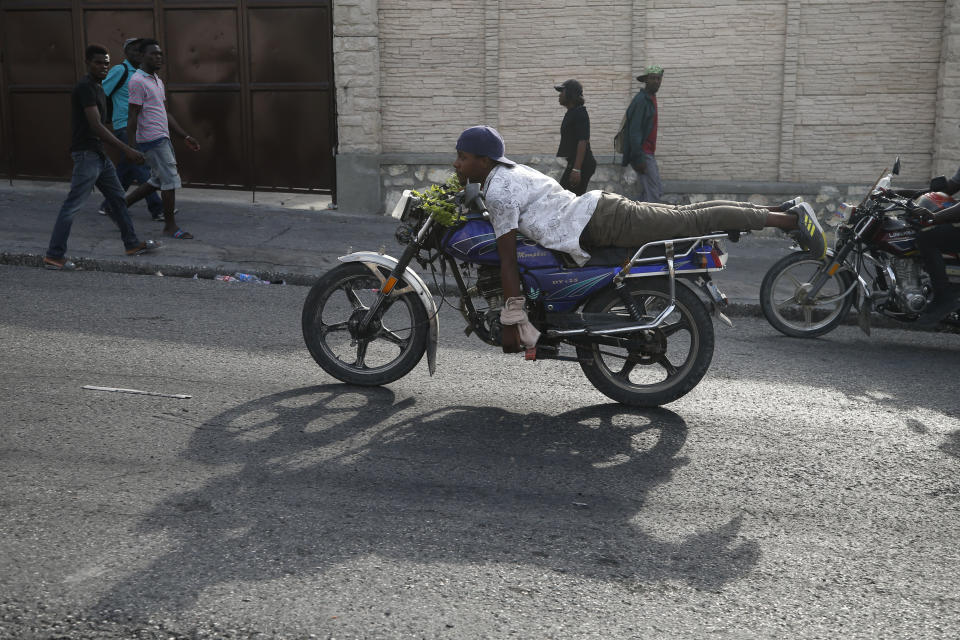 A man rides his motorcycle with no hands as protestors advance toward Petionville after marching past United Nations headquarters, in Port-au-Prince, Haiti, Friday, Oct. 4, 2019. Thousands of protesters marched through the Haitian capital to the U.N. headquarters Friday in one of the largest demonstrations in a weekslong push to oust the embattled President Jovenel Moise. (AP Photo/Rebecca Blackwell)