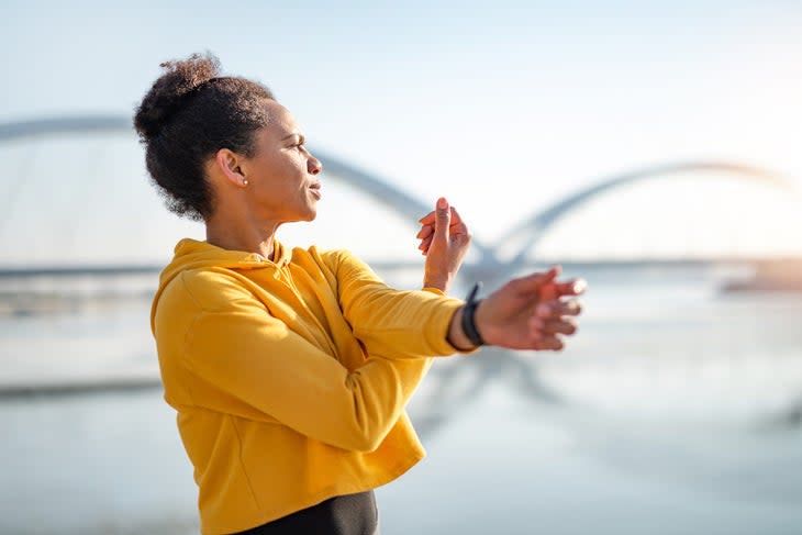 Mid Adult Sporty African American woman doing stretching exercises outdoors next to river early in the morning.