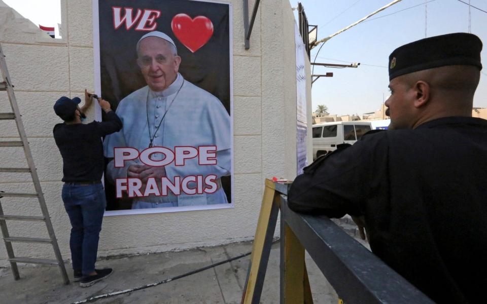 A worker hangs a poster welcoming Pope Francis outside the Cathedral of Saint Joseph in Baghdad - SABAH ARAR /AFP