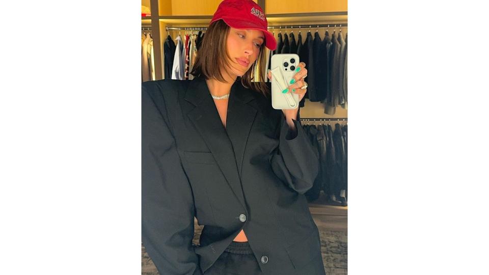 Hailey Bieber poses for a mirror selfie in a black blazer and red cap