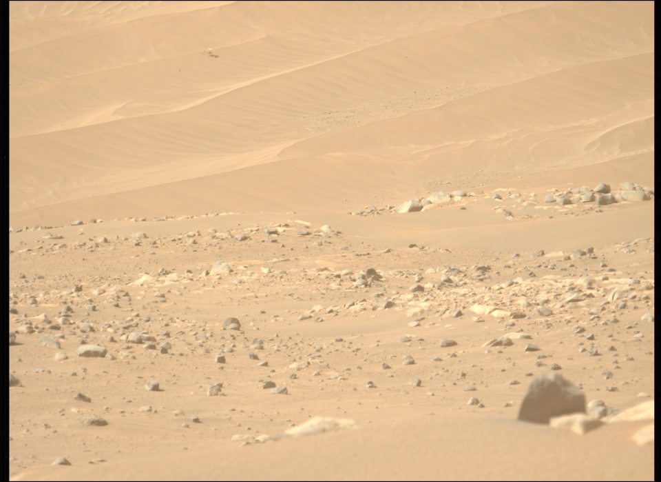 a small helicopter can be seen motionless on a sand dune in the distance as red soil and rocks fills the scene