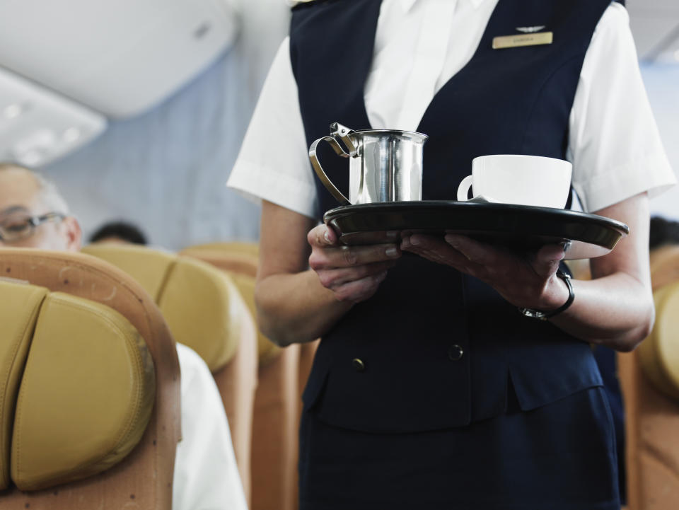 Flight attendant holding tray with coffee, mid section. (PHOTO: Getty Images)