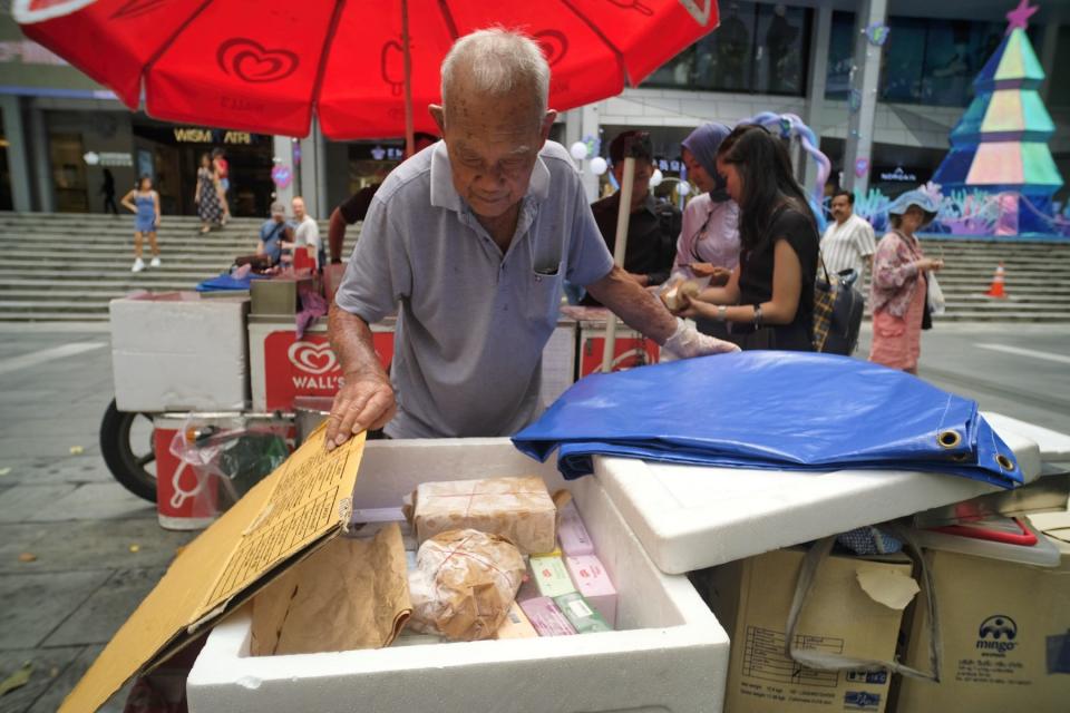 An elderly man looks through a styrofoam cooler box filled with dry ice and ice cream.