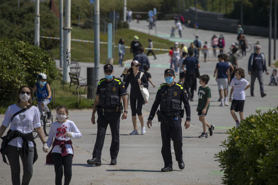 Catalan police officers patrol as families with their children walk along a boulevard in Barcelona, Spain, Sunday, April 26, 2020 as the lockdown to combat the spread of coronavirus continues. On Sunday, children under 14 years old will be allowed to take walks with a parent for up to one hour and within one kilometer from home, ending six weeks of compete seclusion. (AP Photo/Emilio Morenatti)