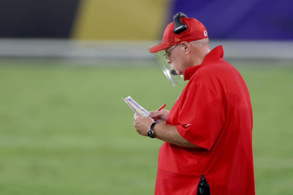 Andy Reid looks down at his playcard while wearing a face shield. 