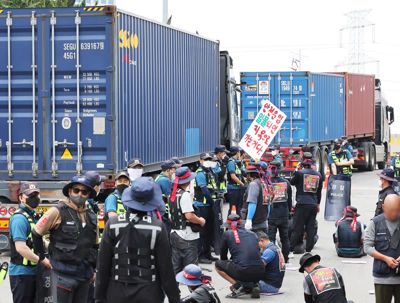 Trucks transporting containers drive past members of the Cargo Truckers Solidarity union gathering in front of an inland containers depot in Uiwang