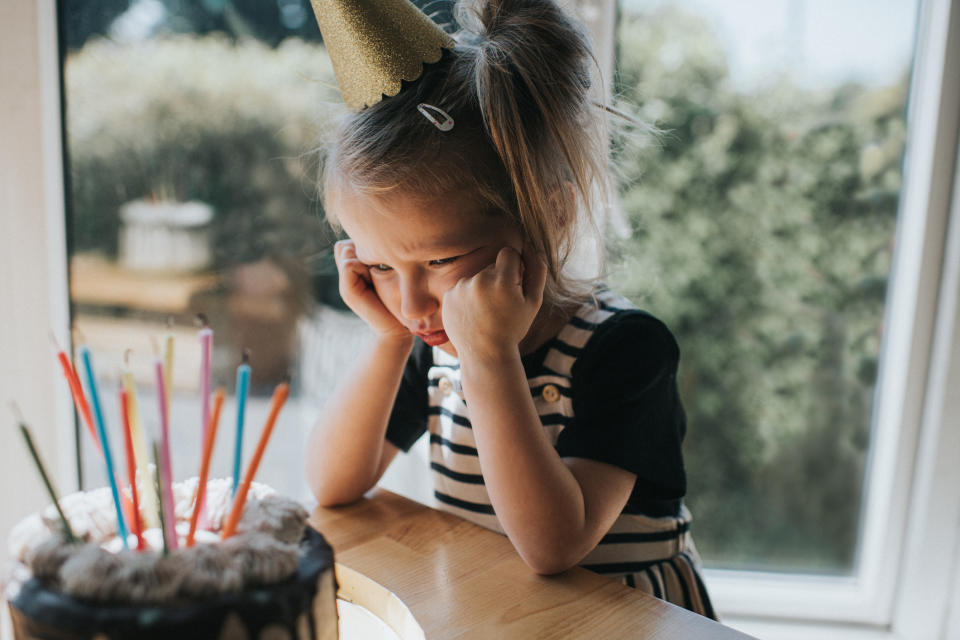 A young girl looking upset while sitting at a table with a birthday cake on it