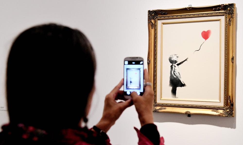 A woman takes picture on May 23, 2016, of a piece entitled “Girl with ballon, red” by England-based graffiti artist Banksy