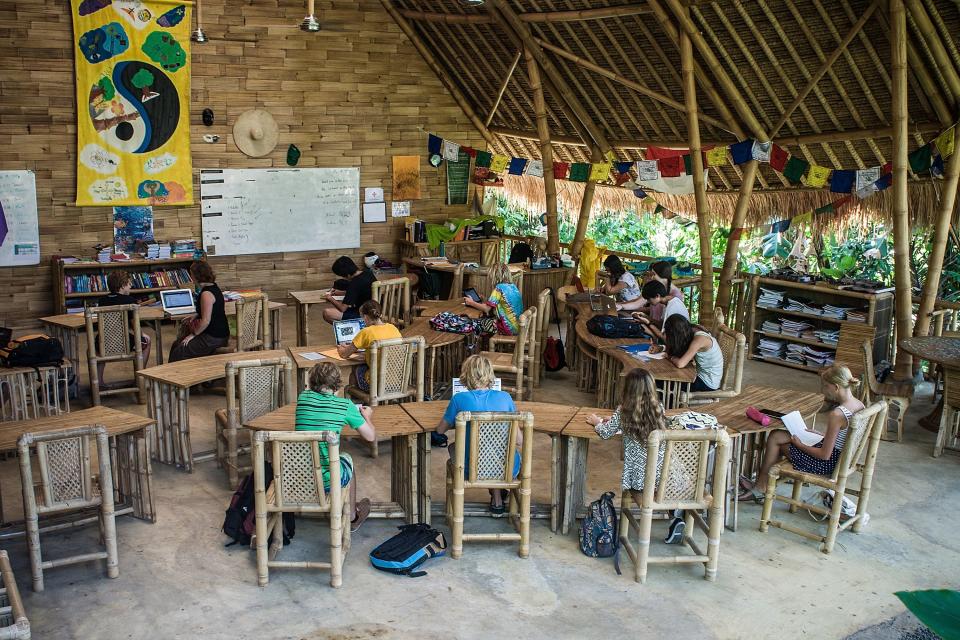 A group of young students sitting at their wooden desks in a bamboo school building in Bali.