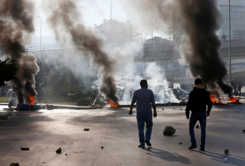 Protestors walk near burning barricades during a protest over economic hardship and lack of new government in Beirut
