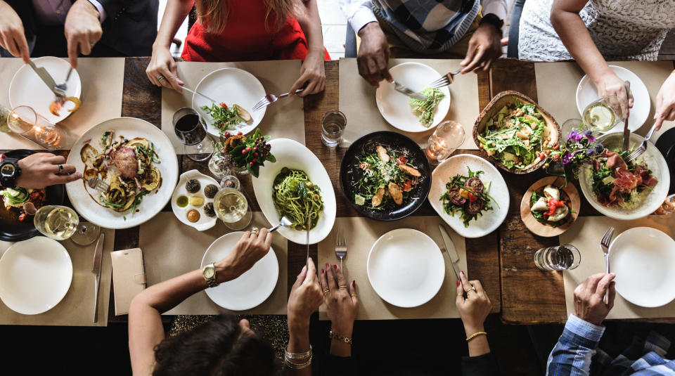 Group of people dining at a table with various dishes, sharing a meal together