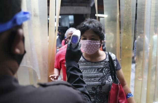 A security guard checks the body temperature of a woman before entering a clothing market to help curb the spread of the coronavirus in Jakarta, Indonesia