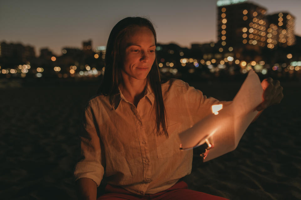 Woman with burning paper sitting on beach at night