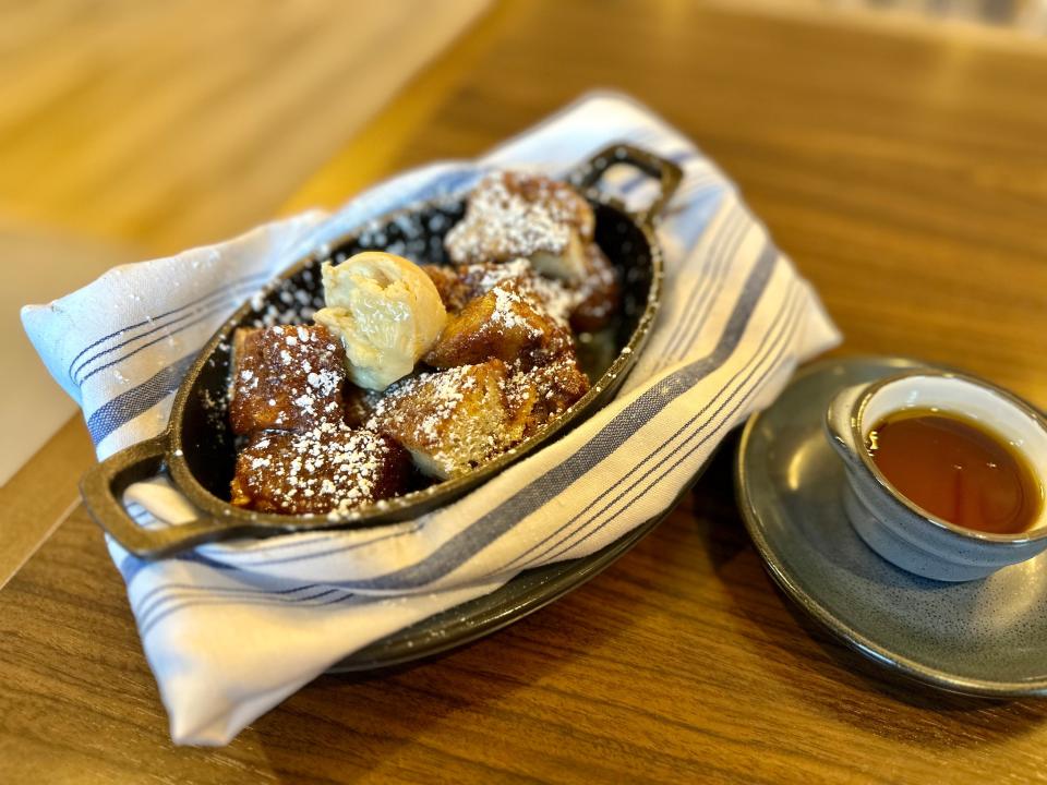 Cast-iron tray of cinnamon bread chunks topped with creamy butter and a side of syrup