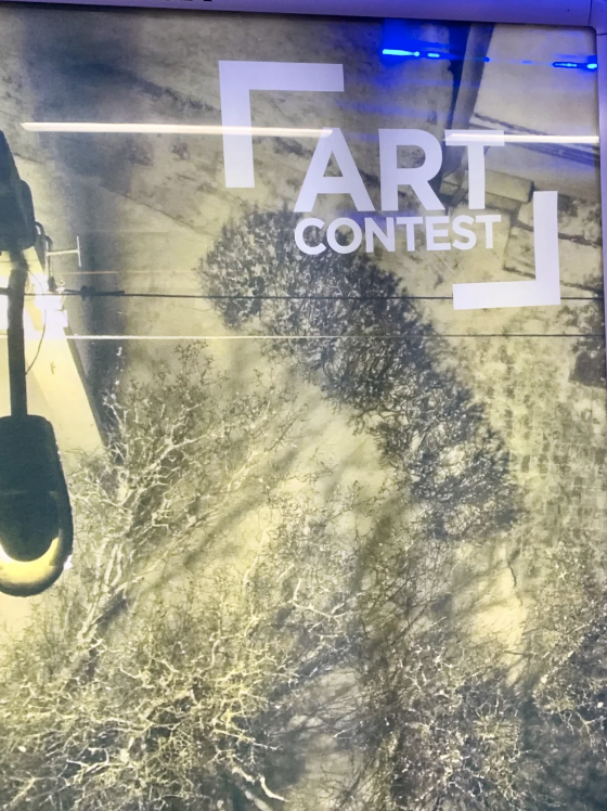 Shadow of a person holding a circular object, projected on a poster advertising an art contest
