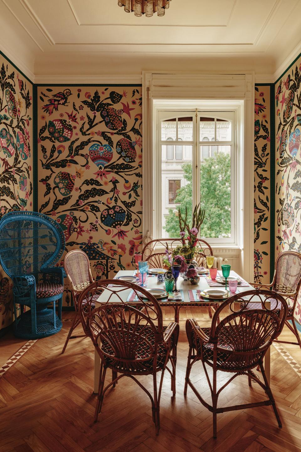 In the dining room, vintage bamboo chairs with cushions of a La DoubleJ fabric surround a white Molteni table set with pieces from La DoubleJ. Custom Tree of Life wallpaper created from an illustration by artist Kirsten Synge based on collages Martin found in Bali.