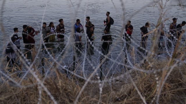 Migrants wait to climb over concertina wire