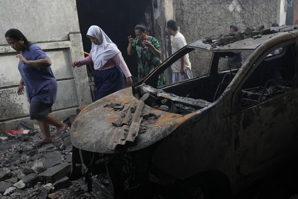 Residents walk past a burned out vehicle at a neighborhood affected by a fuel depot fire in Jakarta, Indonesia, Saturday, March 4, 2023. A large fire broke out at the fuel storage depot in Indonesia's capital Friday, killing multiple people, injuring dozens of others and forcing the evacuation of thousands of nearby residents after spreading to their neighborhood, officials said. (AP Photo/Tatan Syuflana)