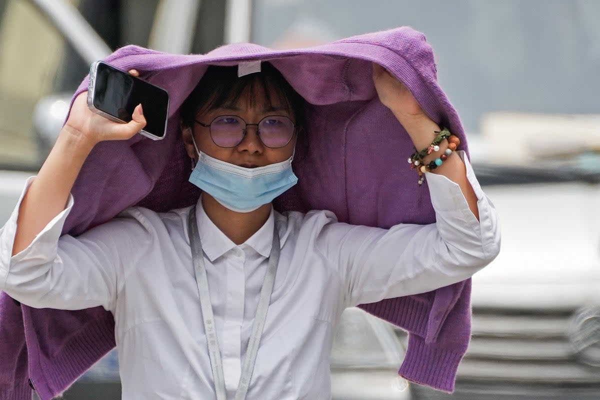 A woman uses a sweater to shield from the sun as she walls on a street on a hot day in Beijing (AP)