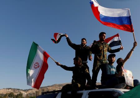 Sirios ondean banderas de su país, Irán y Rusia en una protesta contra los ataques aéreos liderados por Estados Unidos, en Damasco. 14 de abril de 2018. REUTERS/ Omar Sanadiki