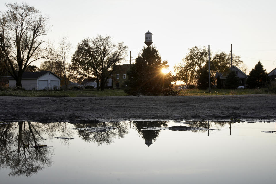 In this Oct. 24, 2019 photo, the setting sun and homes are reflected in a puddle, in Winslow, Neb. It took only minutes for swift-moving floods from the Elkhorn River to ravage tiny Winslow this spring, leaving nearly all its 48 homes and businesses uninhabitable. Now, the couple dozen residents still determined to call the place home are facing a new challenge: Moving the entire town several miles away to higher ground. (AP Photo/Nati Harnik)