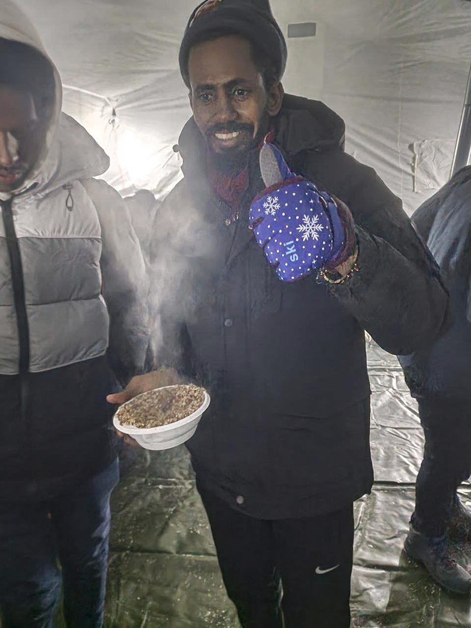 In this handout photo released by Governor of Murmansk region Andrey Chibis' telegram channel on Wednesday, Nov. 22, 2023, a migrant gestures holding a hot meal as other migrants gather getting hot drinks inside a tent near the border with Finland at the Salla checkpoint, one of the still open border checkpoints situated in the Kandalaksha district of the Murmansk region, about 1300 km (812 miles) north of Moscow, Russia. (Governor of Murmansk region Andrey Chibis' telegram channel via AP)