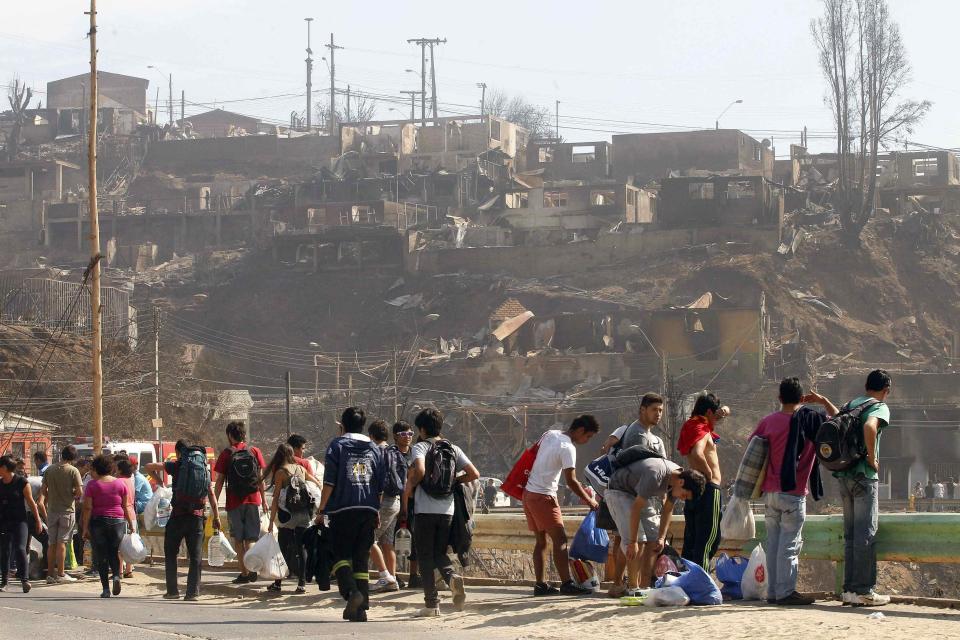 Residents walk carrying their belongings in front of the remains of houses after a forest fire burned several neighbourhoods in the hills in Valparaiso city, northwest of Santiago, April 13, 2014. At least 11 people were killed and 500 houses destroyed over the weekend by a fire that devastated parts of the Chilean port city of Valparaiso, as authorities evacuated thousands and sent in aircraft to battle the blaze. REUTERS/Eliseo Fernandez (CHILE - Tags: SOCIETY ENVIRONMENT DISASTER)