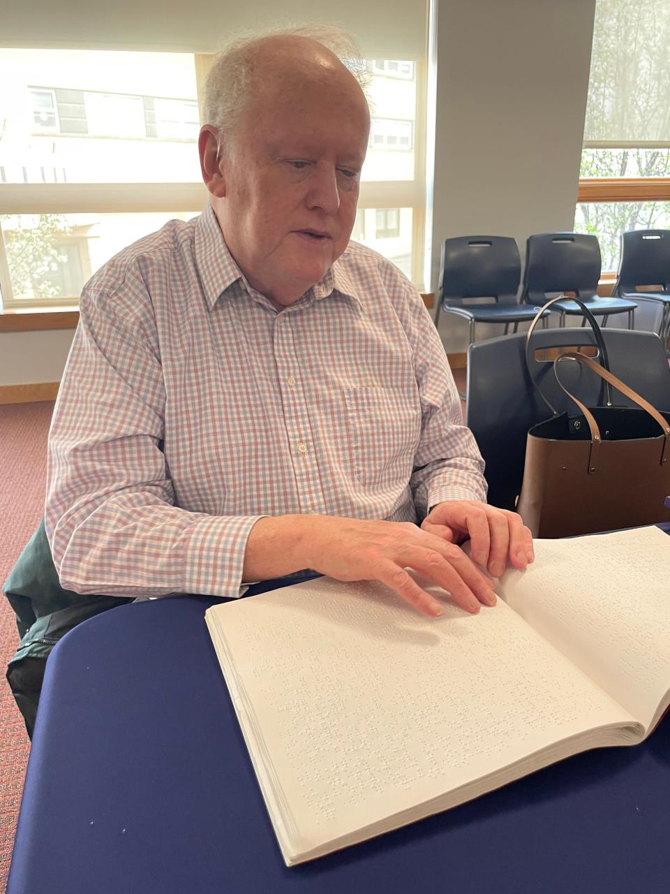 Kevin Harkins, board vice president of the South East CT Community Center of the Blind, reading a braille book. He said braille books are at least two-and-a-half times the size of a regular print book.