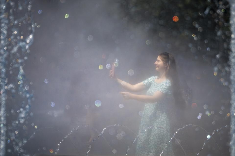A girl take pictures as she is engulfed by mist from a public fountain in Bucharest, Romania, Monday, July 17, 2023. (AP Photo/Andreea Alexandru)