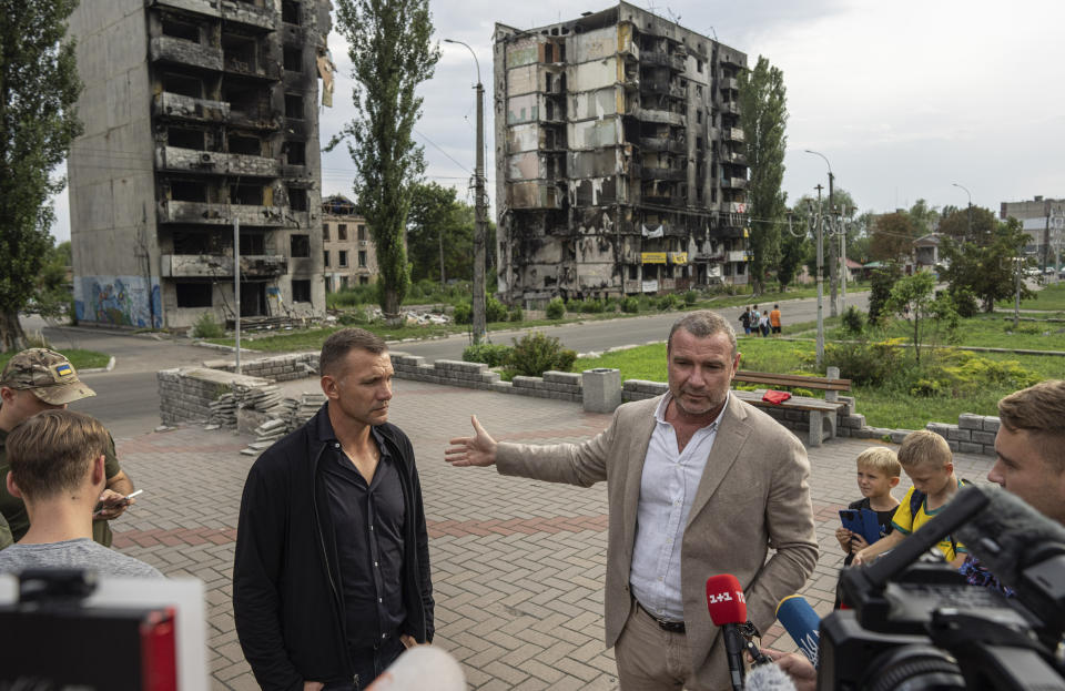 El exfutbolista y entrenador de la selección nacional de Ucrania, Andriy Shevchenko, izquierda, y el actor estadounidense Liev Schreiber hablan con medios de comunicación frente a un edificio destruido por la ofensiva rusa en Borodianka, cerca de Kiev, Ucrania, el 15 de agosto de 2022. (Foto AP/Evgeniy Maloletka)