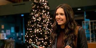 Still from Love Hard where Nina Dobrev smiles in front of a Christmas tree.