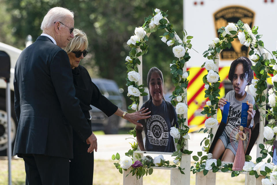 President Joe Biden and first lady Jill Biden stand in front of a memorial made of pictures of children and white flowers.