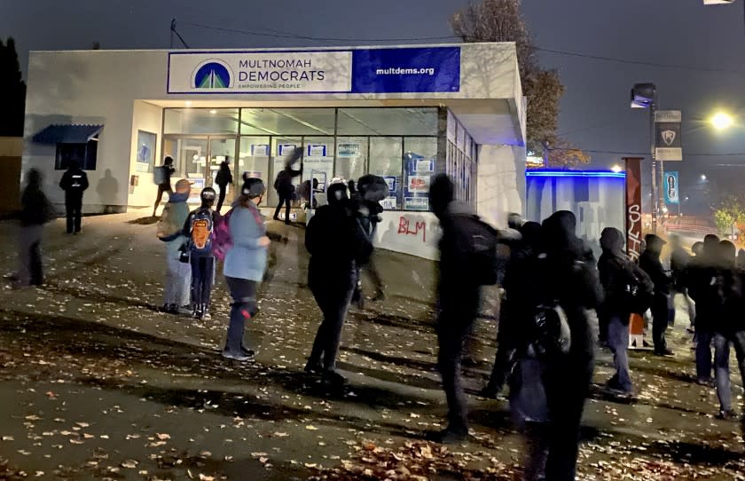 Activists, at rear, break windows Sunday night, Nov. 8, 2020, at the county Democratic Party headquarters in Portland, Ore., after spray-painting "BLM" and an anti-Joe Biden slogan on walls. Black community leaders say the activists have hijacked the protest movement, undermining Black Lives Matter causes. Photo by Brenda Griswold for the Times