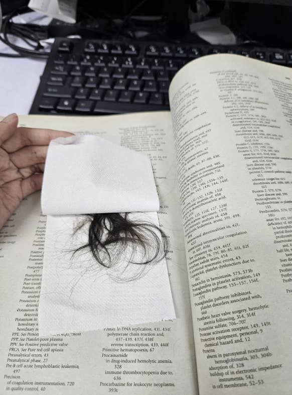 A person's hand is holding a napkin with hair on it, placed on an open scientific textbook