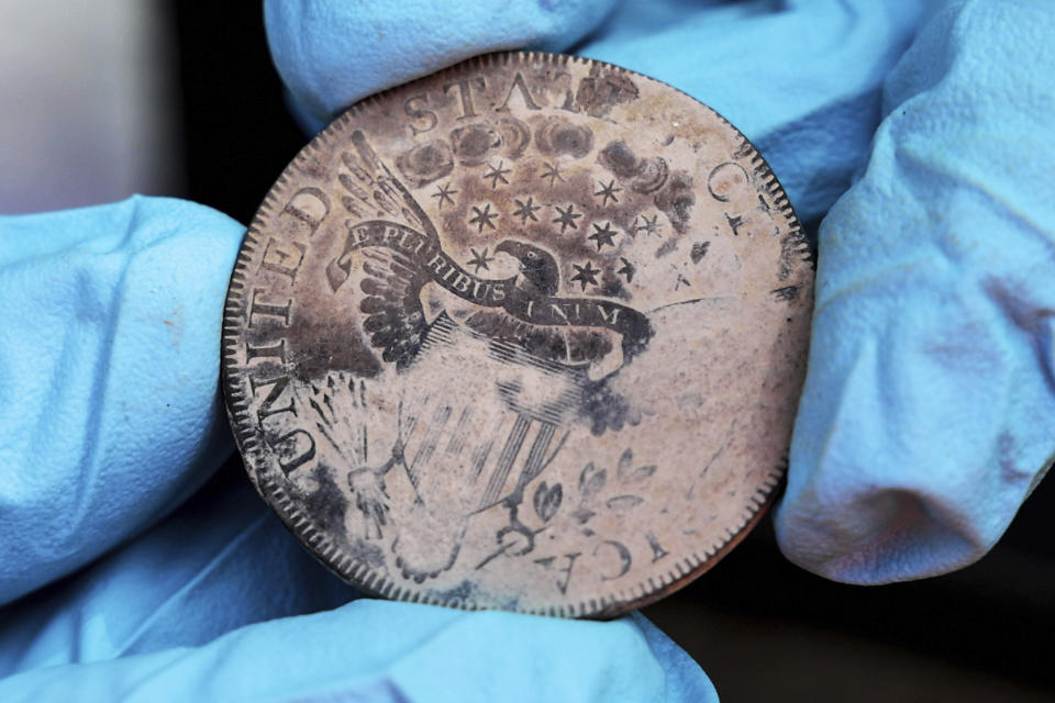 This photo, provided b the U.S. Military Academy at West Point, Aug. 30, 2023, shows West Point archeologist Paul Hudson display an 1800 Draped Bust Dollar, one of the coins found in the lead box believed to have been placed in the base of a monument by cadets almost two centuries ago, in West Point, NY. The nearly 200-year-old West Point time capsule, that appeared to yield little more than dust when it was opened during a disappointing livestream earlier this week, contained hidden treasure after all, the U.S. Military Academy said Wednesday. (U.S. Military Academy at West Point via AP)