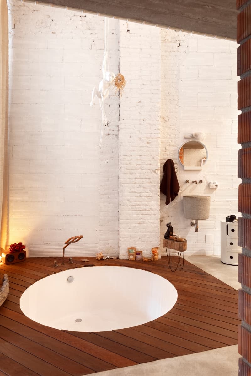 round bathtub set in wood floor in white brick bathroom