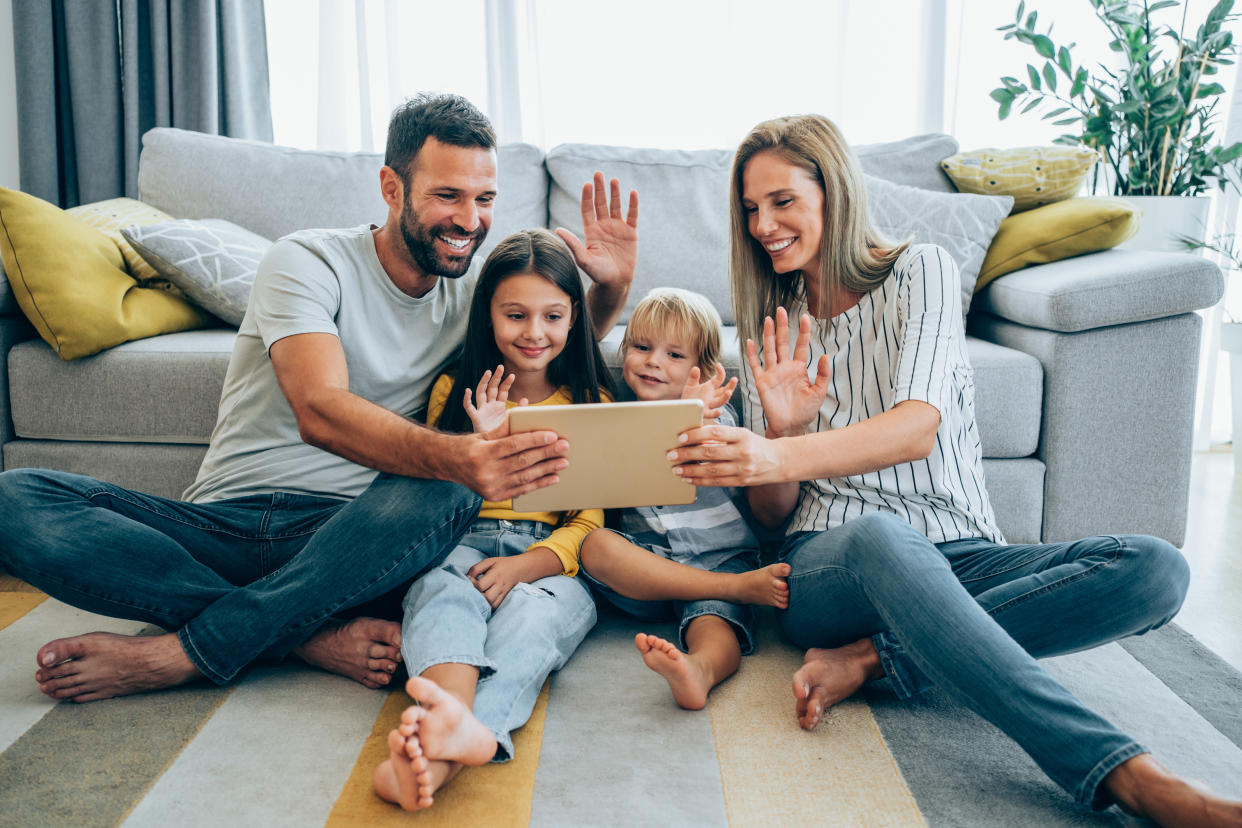 Shot of a smiling family with two kids using digital tablet on the sofa at home. Happy young family making video call with tablet at home.